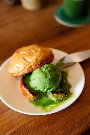 Scoop of Matcha green tea ice cream with bun bread on wooden table. Selective focus.