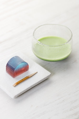 Cup of fresh matcha tea, green tea and Kingyoku can, traditional Japanese jelly confectionery on white wooden table. Selective focus.の写真素材