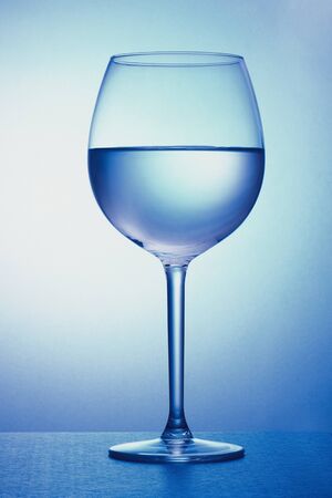 glass of wine half filled with water with blue lightingの写真素材