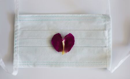 Medical mask on white background with rose petal in heart shapeの写真素材