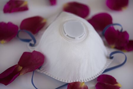 Medical face mask with scattered rose petals on white backgroundの写真素材