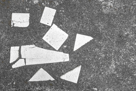 Broken white tile pieces scattered in abstract design on concrete pavementの写真素材