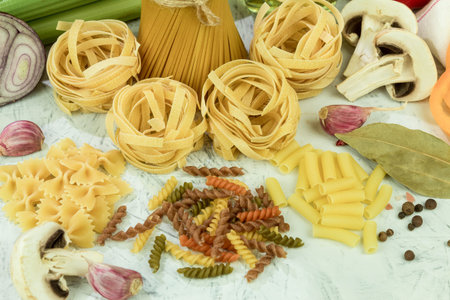 Assorted different types of pasta on the table. Various types of raw pasta and noodles with vegetables. Culinary concept of Italian cuisine. Collection of various raw pasta on the kitchen tableの写真素材