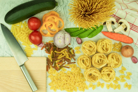 Assorted different types of pasta on the table. Various types of raw pasta and noodles with vegetables. Culinary concept of Italian cuisine. Collection of various raw pasta on the kitchen tableの写真素材