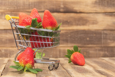 Fresh strawberries in a shopping cart on a wooden background. Lots of ripe sweet strawberries in a basket. Close-up. Side view and space for textの写真素材
