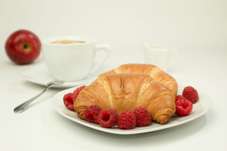 Breakfast with a cup of coffee, fresh croissants and ripe berries on a white wooden background. Background with space for text, copy space. Croissants with coffee and delicious, fresh raspberriesの写真素材