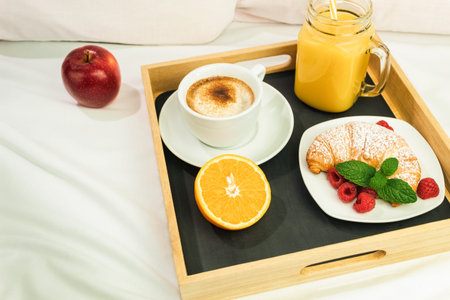 Coffee, orange juice and a croissant on a wooden stalk. Romantic breakfast in bed on white sheets,...