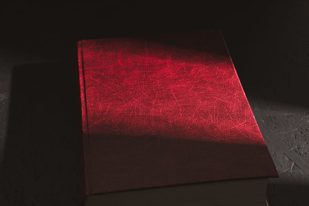 An old red book, A hard ray of the sun falls on an old red book. Sunbeam on the book. Close-up
