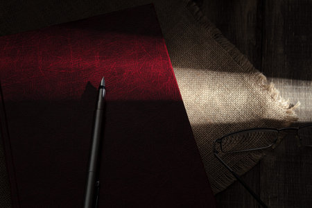 A hard ray of sun falls on an old red book. Sunbeam in the dark, on a book. Close-up. Old red book