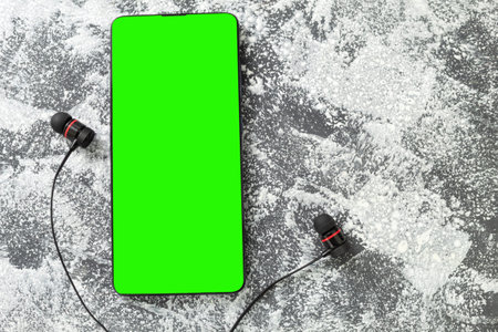 Mockup of a mobile phone with a chroma key screen. Smartphone with headphones on the table. Copy...
