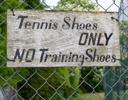 Old sign with peeling paint indicating that tennis shoes only should be wornの写真素材