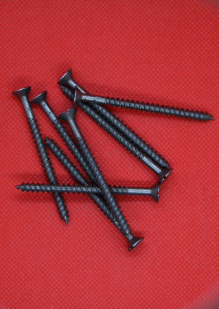 Pile of grey metal screws on red background with space for copy