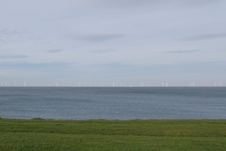 View of wind farm turbines on horizon with sea and grass in foregroundの写真素材