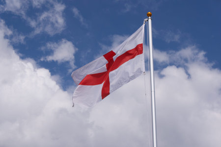 Red and white flag of St George England against blue cloudy sky