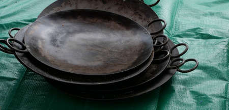 Flat worn cast iron Indian cuisine cooking pans with handles on green tarpaulinの写真素材