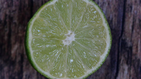 Fresh juicy green slice of lime against textured wooden background