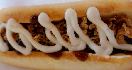 Top view of hot dog in white bun with toppings including mayonnaise