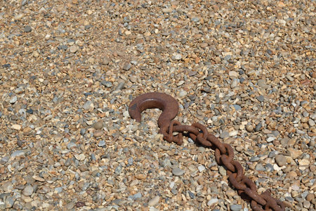 Old rusty orange brown nautical chain with hook lying on shingle beach