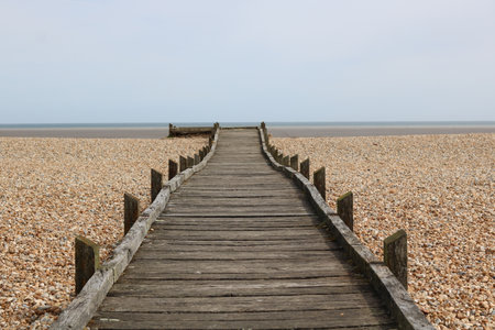 Weathered wooden board walk or path leading across shingle beach to the seaの写真素材