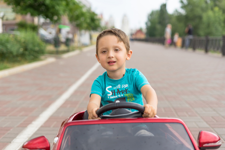 Smiling little boy driving by toy car. Active leisure and sports for kids. Portrait of happy little kid on the street. Funny cute children making vacations and enjoying summer. Healthy lifestyle.の写真素材
