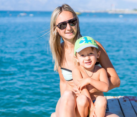 Young smiling mother and baby boy son playing on the beach in the day timeの写真素材