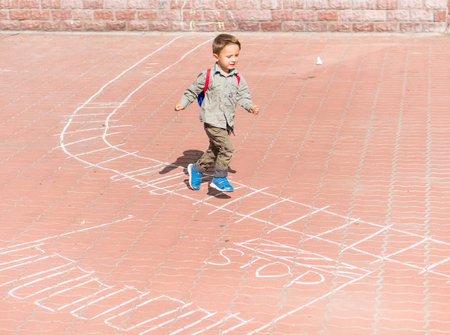 The boy runs to the drawings on the pavement. Cute kid boy drawing with chalk on the pavement in the...