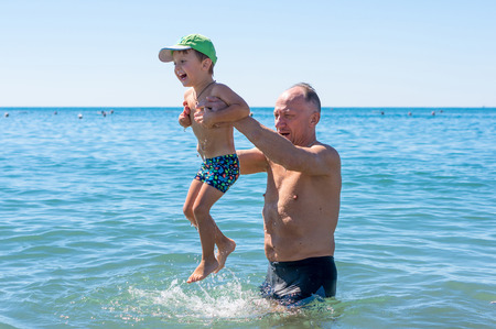 Smiling grandfather and grandson playing at the seaの写真素材
