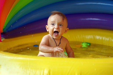 Boy playing in inflatable baby pool. Kid swim and splash in colorful garden play center. Happy boy playing with water toys on hot summer day.の写真素材