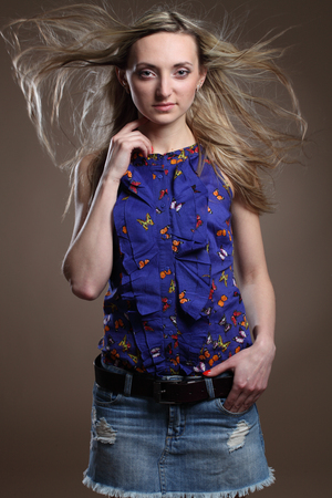 Portrait of a beautiful young adult slim sexy and attractive sensuality pretty blonde woman in blue elegance fashionable shorts and blouse isolated on brown backgroundの写真素材