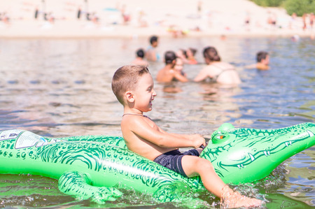 Smiling little baby boy are playing with a toy crocodile in the lakeの写真素材