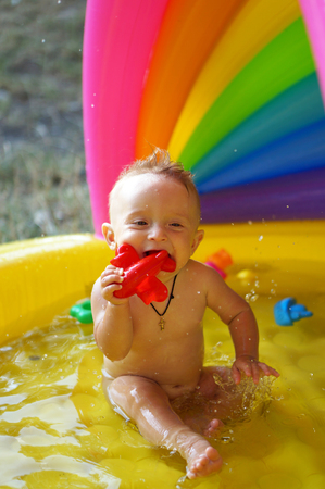 Boy playing in inflatable baby pool. Kid swim and splash in colorful garden play center. Happy boy playing with water toys on hot summer day.                     の写真素材