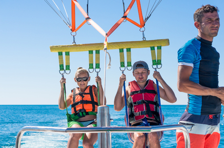 Happy couple Parasailing in Dominicana beach in summer. Couple under parachute hanging mid air. Having fun. Tropical Paradise. Positive human emotions, feelings, family, children, travel, vacation. Spring and summer holidays.の写真素材