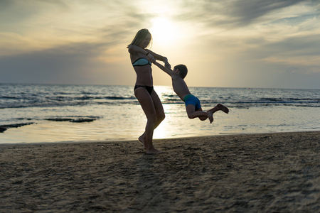 Young mother and smiling baby boy son playing on the beach on the Sunset. Positive human emotions, feelings, joy. Funny cute child making vacations and enjoying summer. Spring and summer holidays.の写真素材