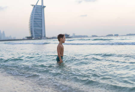 Portrait smiling little baby boy playing in the sea, ocean. Positive human emotions, feelings, joy. Funny cute child making vacations and enjoying summer. Sunset Dubai beach.の写真素材