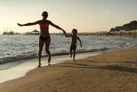Young mother and smiling baby boy son playing on the beach on the Sunset. Positive human emotions, feelings, joy. Beautiful summer sunny day, blue sea, picturesque landscape. Majorca, Spainの写真素材