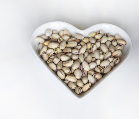 Nuts arranged in heart  on background. Healthy Food image close up pistachios on the cup plate. Love Texture on white grey table top view mock upの写真素材