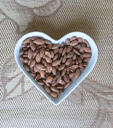 Nuts arranged in heart  on background. Healthy Food image close up almond on the cup plate. Love Texture on top view mock upの写真素材