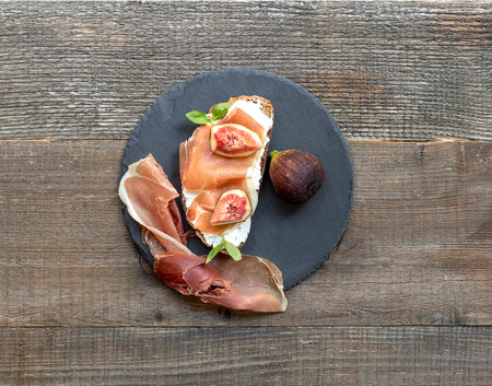 Sandwich with Italian prosciutto crudo and figs on the old wooden table. Top view, round plate.