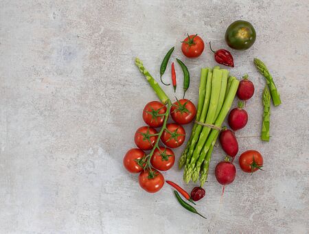 Top view of organic vegetables on white background. Green asparagus, tomatoes, radish, chili peppers. Flat lay, copy spaceの写真素材