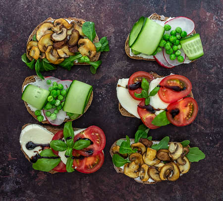 Open vegetarian toasts with different toppings, top view. Flat lay of rye bread crostini with mushrooms, tomatoes, cucumbers.の写真素材