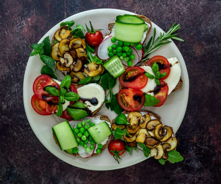 Plate with vegetarian sandwich toasts with different toppings, top view. Flat lay of rye bread crostini with mushrooms, tomatoes, cucumbers.の写真素材