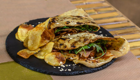 Piadina Romagnola. Fast Italian food, take away food. Flat sandwich with beef, bacon, and arugula.
