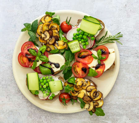 Plate with vegetarian sandwich toasts with different toppings, top view. Flatlay of rye bread crostini with mushrooms, tomatoes, cucumbers.の写真素材