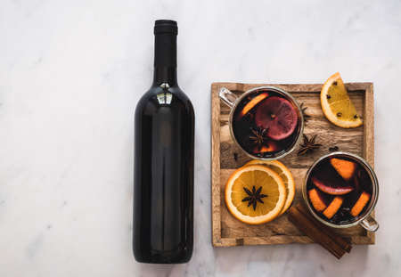 Hot holiday drink mulled wine with oranges, gloves, anise stars, and cinnamon. Wooden tray, bottle of wine, copy space for text.の写真素材