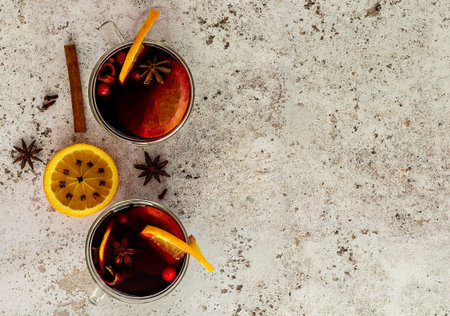 Two glasses of hot mulled wine with oranges and spices with Christmas lights and decorations.