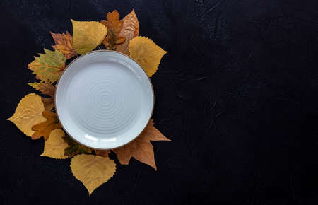 Autumn and Thanksgiving day table setting with fallen leaves and the empty white plate on the dark backgroundの写真素材
