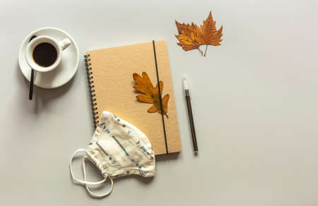 Workspace with notebook, mask, pen, autumn leaves, and coffee cup. Flat lay, top view table desk. New normalityの写真素材