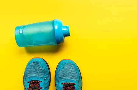Flat lay sport shoes and a bottle of water on a yellow background. Concept of a healthy lifestyle and fitness.の写真素材