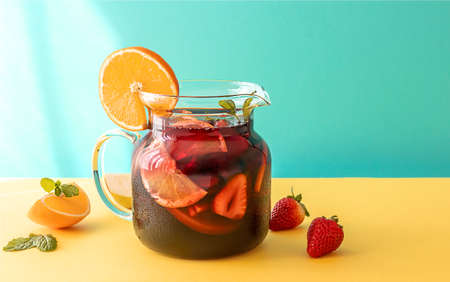 Summer cold cocktail, fruit and berry red wine sangria with apple, lemon, oranges, and strawberry. blue and yellow background, copy space.の写真素材
