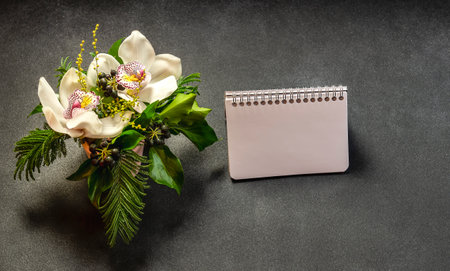 Orchid bouquet and blank notebook paper on black background. Free space for message.の写真素材